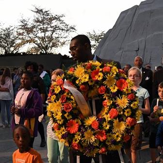 A man surrounded by people, holding a colorful wreath of yellow and orange flowers